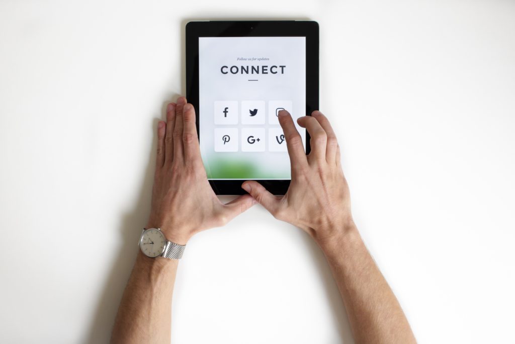 Caucasian hands hold a tablet that reads Connect and has the symbol of the most known social networks. Digital presence can be improved with a new website..